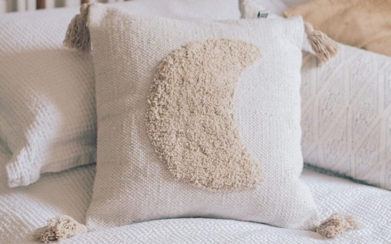Photo of a cushion with a moon and tassels on a bed